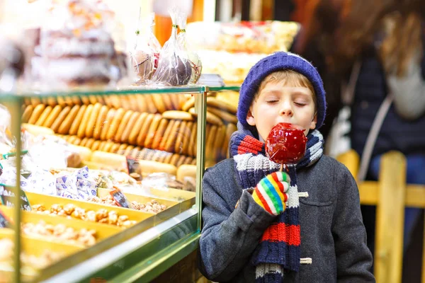 Criança feliz comendo na maçã coberta com açúcar vermelho no mercado de Natal — Fotografia de Stock