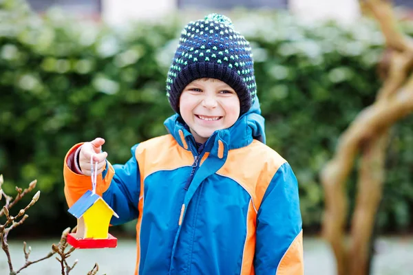 Little kid boy hanging bird house on tree for feeding in winter — Stock Photo, Image