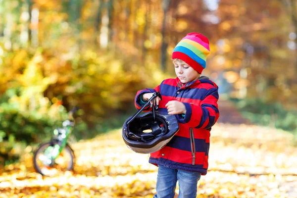 Aktives Kind setzt vor dem Radfahren an sonnigen Herbsttagen in der Natur sicheren Helm auf. — Stockfoto