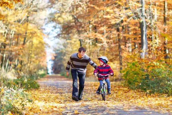 Kleiner Junge und sein Vater parken im Herbst mit einem Fahrrad. Papa bringt seinem Sohn Radfahren bei — Stockfoto