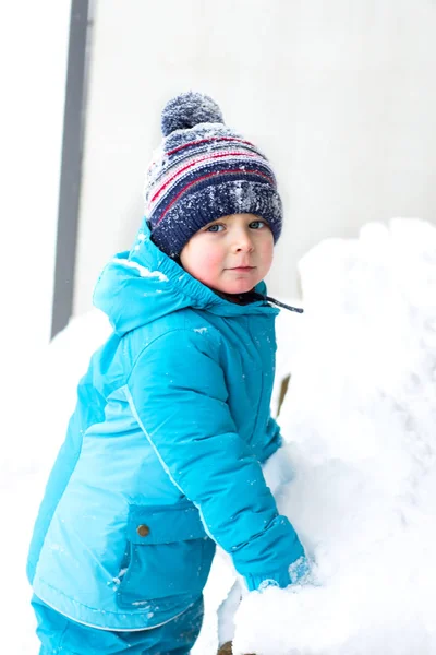 Winter portrait of kid boy in colorful clothes, outdoors during snowfall. Active outdoors leisure with children in winter on cold snowy days — Stock Photo, Image