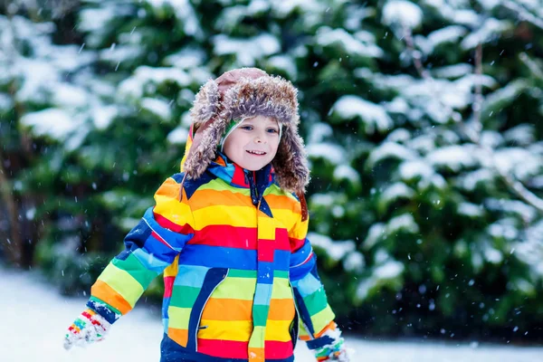 Cute little funny kid boy in colorful winter fashion clothes having fun and playing with snow, outdoors during snowfall — Stock Photo, Image