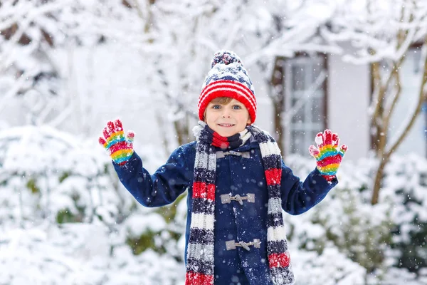 Engraçado menino em roupas coloridas jogando ao ar livre durante forte queda de neve — Fotografia de Stock