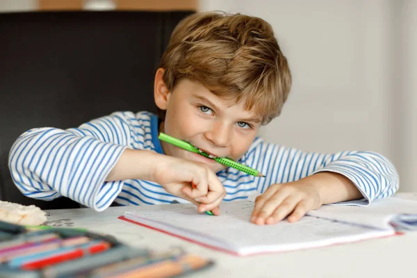 Porträt eines süßen gesunden, glücklichen Schuljungen, der zu Hause Hausaufgaben macht. Kleines Kind schreibt mit Buntstiften, drinnen. Grundschule und Bildung. Kind lernt Buchstaben und Zahlen schreiben — Stockfoto