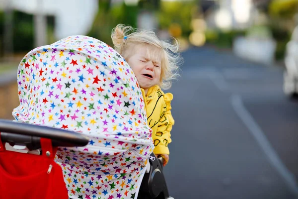 Retrato de uma menina pequena e triste sentada no carrinho e indo dar um passeio. Criança chorando não quer sentar no carrinho. Filha saudável. Crise histérica de dois anos de fase — Fotografia de Stock
