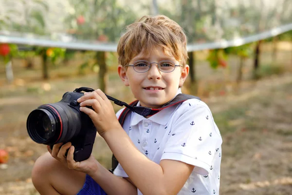Beautiful kid boy with glasses making pictures by using digital professional camera. Little child learning to be creative and taking photograph. Outdoors shooting and photosession — Stock Photo, Image