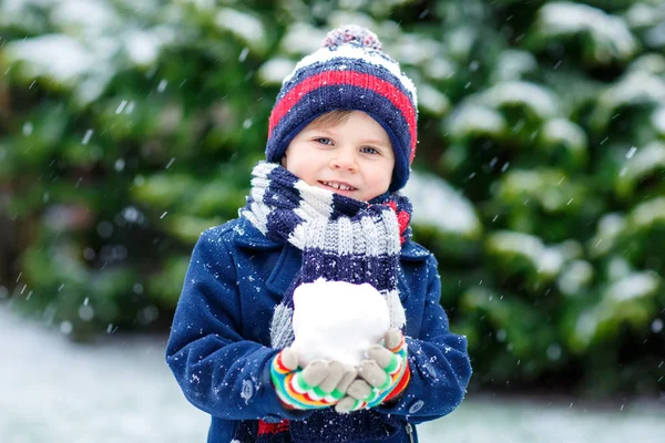Søt liten spøkefugl i fargerike vintermoteklær, morsomme og lekte med snø, utendørs under snøfall. – stockfoto