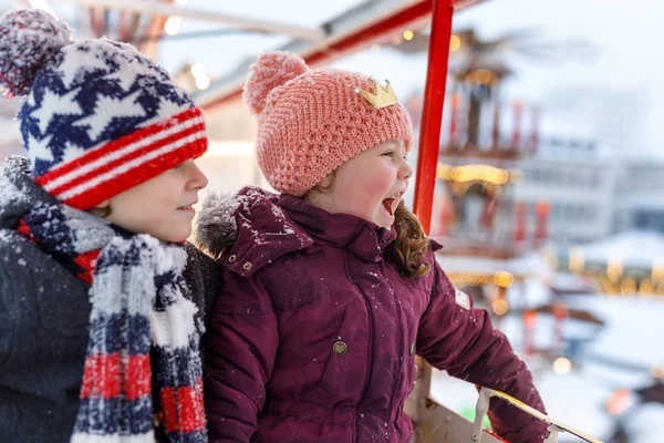 Duas crianças pequenas, menino e menina se divertindo na roda gigante no tradicional mercado de Natal alemão durante a forte queda de neve — Fotografia de Stock