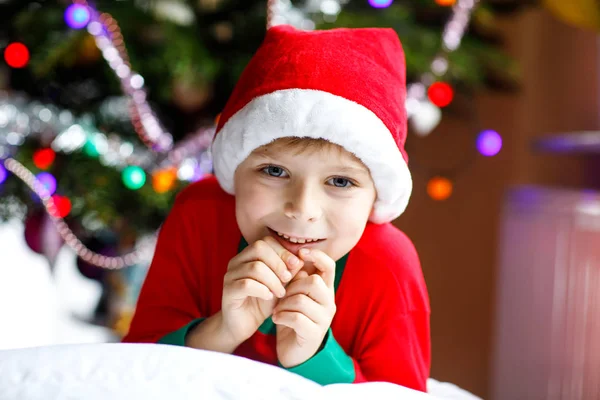 Liten unge pojke i Tomtemössa med julgran och lamporna på bakgrunden. — Stockfoto