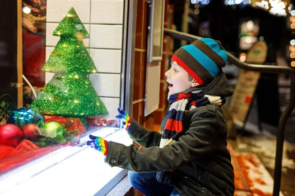 Komik mutlu çocuk moda kış giysileri pencere alışveriş yapma hediyeler, xmas ağacı ile dekore edilmiştir. — Stok fotoğraf