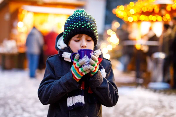 Little cute kid boy drinking hot children punch or chocolate on German Christmas market. Happy child on traditional family market in Germany, Laughing boy in colorful winter clothes — Stock Photo, Image