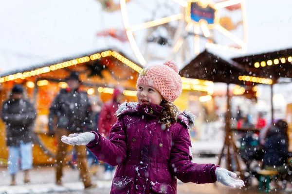 Little cute kid girl having fun on traditional Christmas market during strong snowfall. Happy child enjoying traditional family market in Germany — Stock Photo, Image