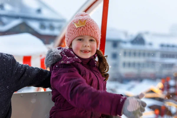 Piccola ragazza carina che si diverte sulla ruota panoramica sul tradizionale mercato di Natale tedesco durante una forte nevicata . — Foto Stock