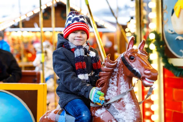 Adorable little kid boy riding on a carousel horse at Christmas funfair or market, outdoors. — Stock Photo, Image