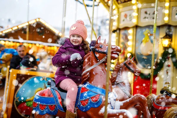 Adorable little kid girl riding on a carousel horse at Christmas funfair or market, outdoors.