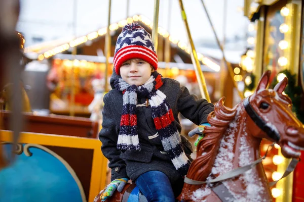 Очаровательный маленький мальчик катается на карусели на рождественской ярмарке или ярмарке, на открытом воздухе . — стоковое фото