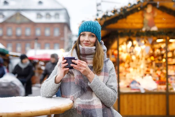 Güzel genç kadın sıcak panç içiyoruz mulled şarap Alman Noeli piyasada. Kış giysileri kış kar günü arka planda Hanau, Almanya ışıkları ile mutlu kızı