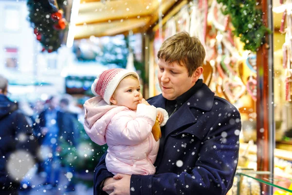 Vader van middelbare leeftijd houdt dochtertje bij zoete stand met peperkoek en noten. Gelukkige familie op kerstmarkt in Duitsland. Schattig meisje dat koekjes eet genaamd Lebkuchen. Feestdag kerstvakantie. — Stockfoto