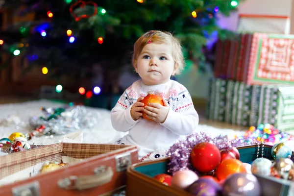 Adorável bebê menina segurando colorido vintage xmas brinquedos e bola em mãos bonitos. Criança em roupas festivas decorando a árvore de Natal — Fotografia de Stock