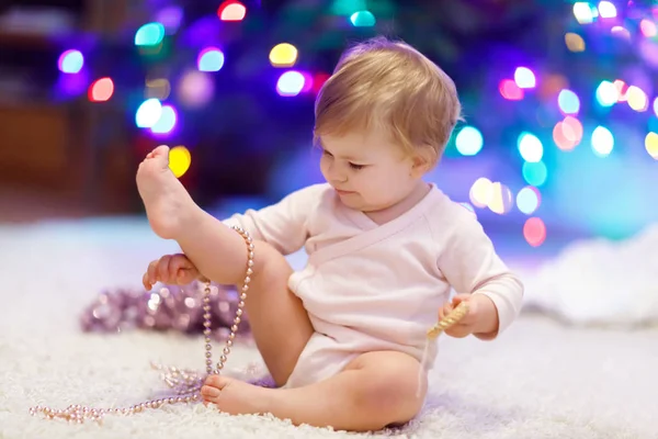 Entzückendes kleines Mädchen mit bunten Lichtergirlanden in niedlichen Händen. Kleines Kind in festlicher Kleidung schmückt Weihnachtsbaum — Stockfoto