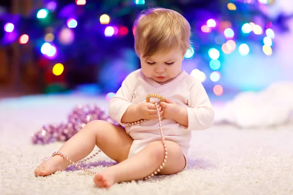 Adorable niña sosteniendo luces coloridas guirnalda en manos lindas. Niño pequeño en ropa festiva decorando el árbol de Navidad — Foto de Stock