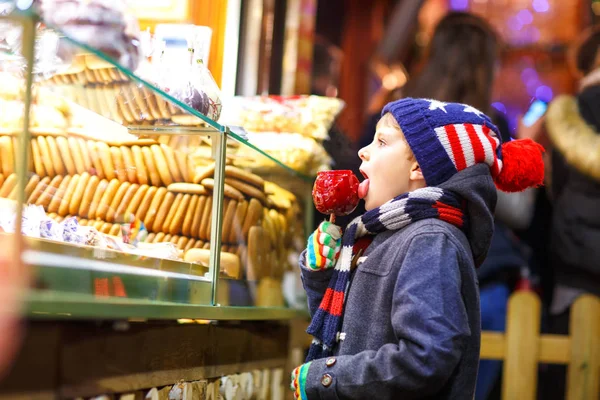 Glückliches Kind isst auf dem Weihnachtsmarkt auf mit rotem Zucker überzogenem Apfel — Stockfoto