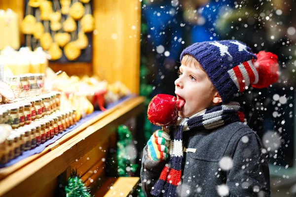 Malé dítě chlapec jí sugar apple sladkosti stojí na vánoční trh — Stock fotografie