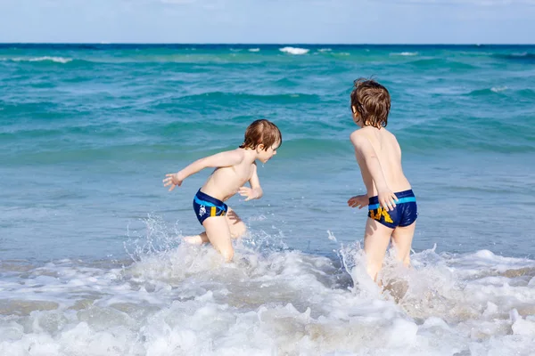 Okyanus plaj üzerinde çalışan iki çocuk çocuklar. Küçük çocuklar eğleniyor