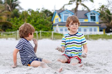 İki küçük bina kum kale ile eğleniyor tropikal kumsalda çocuklar çocuk