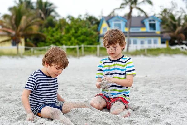 Due bambini piccoli ragazzi si divertono con la costruzione di castello di sabbia sulla spiaggia tropicale — Foto Stock