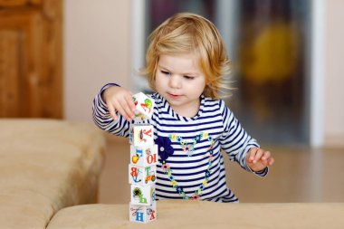 Bebek odasında eğitici oyuncaklarla oynayan tatlı bir kız. Mutlu sağlıklı çocuk evde renkli farklı plastik bloklarla eğleniyor. Sevimli bebek öğrenimi yaratma ve inşa etme