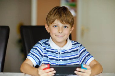 Mutlu küçük çocuk çocuk oyun kumandası ile oynuyor. Çocuk evde internet konsolu aracılığıyla arkadaşlarınızla oyun.