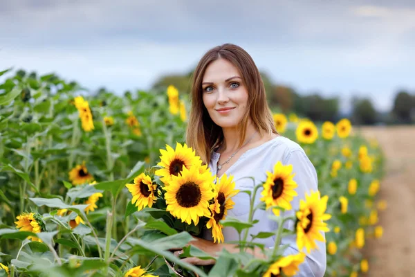Gyönyörű fiatal nő a napraforgó mezőn csokor virágokkal. Boldog lány a nyári naplemente napján. — Stock Fotó