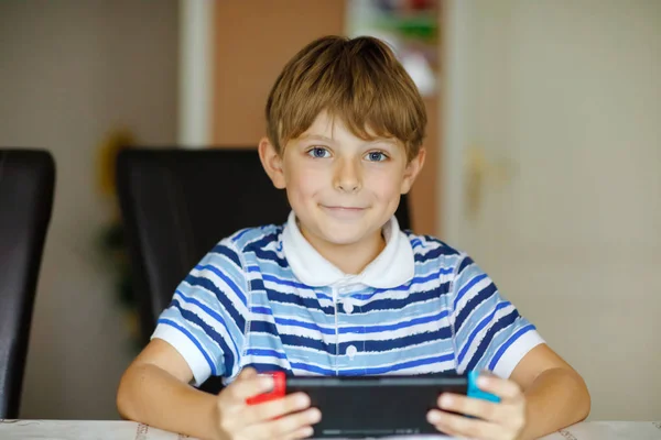 Happy little kid boy playing with game controller. Child gaming with friends at home via internet console.