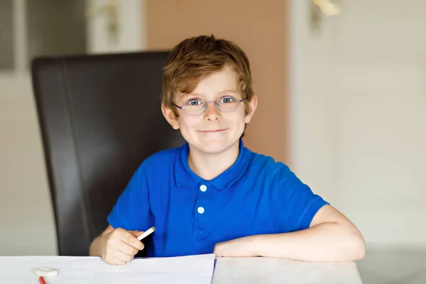 Söt liten unge pojke med glasögon hemma att göra läxor, skriva brev med färgglada pennor. — Stockfoto