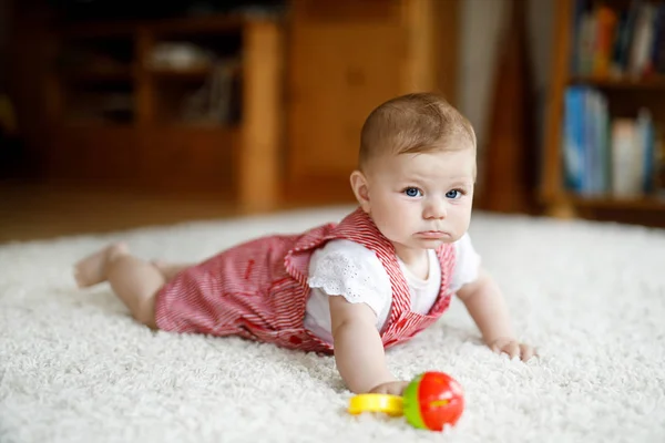 Niedliches Baby, das mit buntem Rasselspielzeug spielt. Kleines Mädchen blickt in die Kamera und krabbelt — Stockfoto