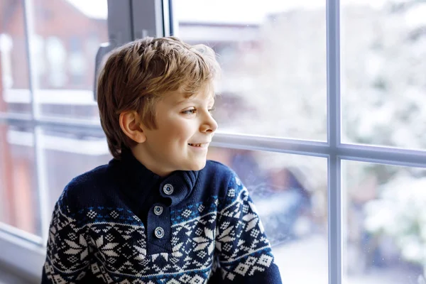 Joyeux adorable garçon enfant assis près de la fenêtre et regardant dehors sur la neige le jour de Noël ou le matin . — Photo