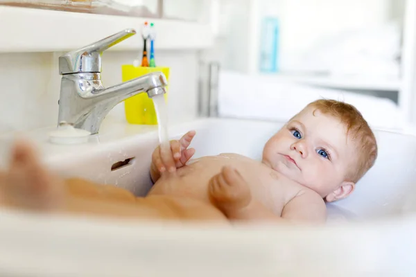 Roztomilý rozkošné dítě brát koupel v mycí dřez a chytit vodovodní kohoutek. — Stock fotografie