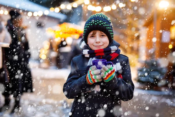 Little cute kid boy drinking hot children punch or chocolate on German Christmas market. Happy child on traditional family market in Germany, Laughing boy in colorful winter clothes — Stock Photo, Image