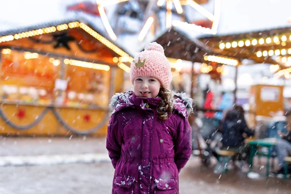 Mała dziewczynka słodkie dziecko, zabawy na tradycyjny jarmark bożonarodzeniowy niemiecki podczas silnych opadów śniegu. — Zdjęcie stockowe