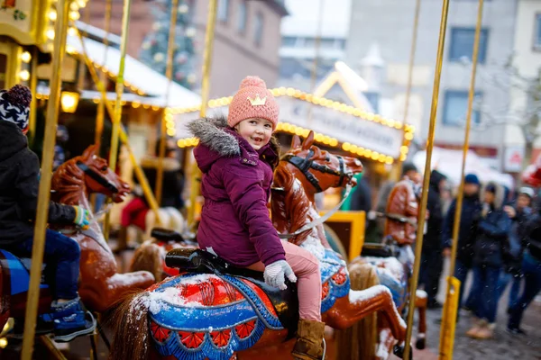 Adorable little kid girl riding on a carousel horse at Christmas funfair or market, outdoors. — Stock Photo, Image