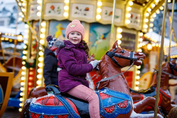 Adorable niña montado en un caballo de carrusel en la feria o mercado de Navidad, al aire libre . — Foto de Stock