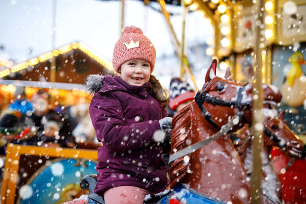 Adorable little kid girl riding on a carousel horse at Christmas funfair or market, outdoors.