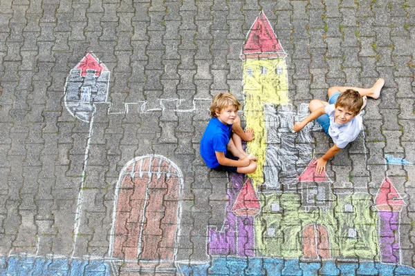 Two little kids boys drawing knight castle with colorful chalks on asphalt. Happy siblings and friends having fun with creating chalk picture and painting. Creative leisure for children in summer. — Stock Photo, Image
