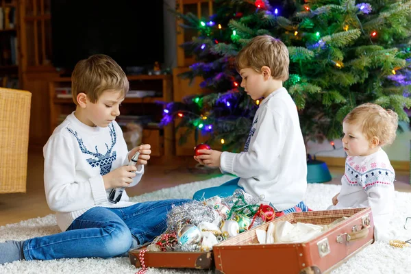 Dois meninos pequenos e adorável bebê menina decoração árvore de Natal com velhos brinquedos vintage e bolas . — Fotografia de Stock