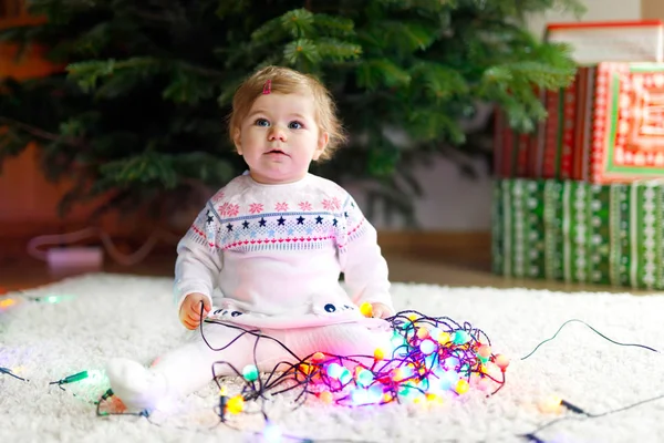 Αξιολάτρευτο κοριτσάκι κρατώντας πολύχρωμα φώτα γιρλάντα στο χαριτωμένο χέρια. Μικρό παιδί σε γιορτινά ρούχα διακόσμησης χριστουγεννιάτικου δέντρου — Φωτογραφία Αρχείου