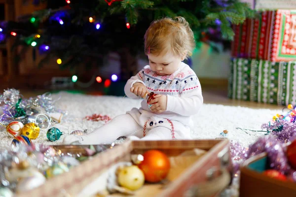 Entzückendes Baby-Mädchen mit buntem Vintage-Weihnachtsspielzeug und Ball in süßen Händen. Kleines Kind in festlicher Kleidung schmückt Weihnachtsbaum — Stockfoto