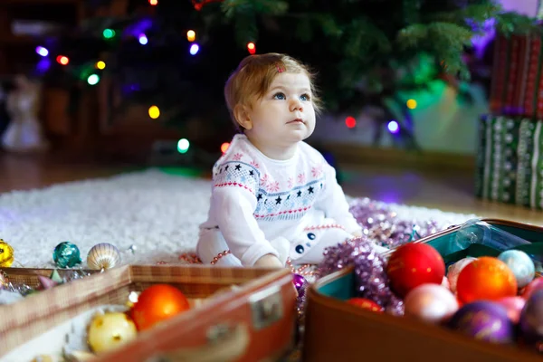 Bedårande flicka håller färgglada vintage xmas leksaker och bollen i söt händer. Litet barn i festliga kläder utsmyckning julgran — Stockfoto