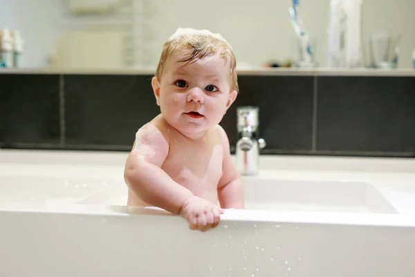 Lindo bebé adorable tomando baño en lavabo y jugando con agua y espuma —  Fotos de Stock