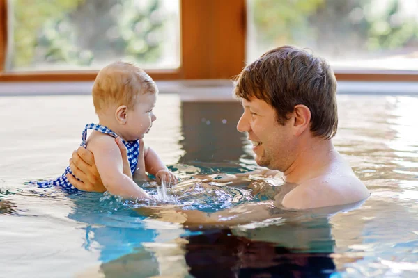 Happy middle-aged father swimming with cute adorable baby girl in swimming pool.